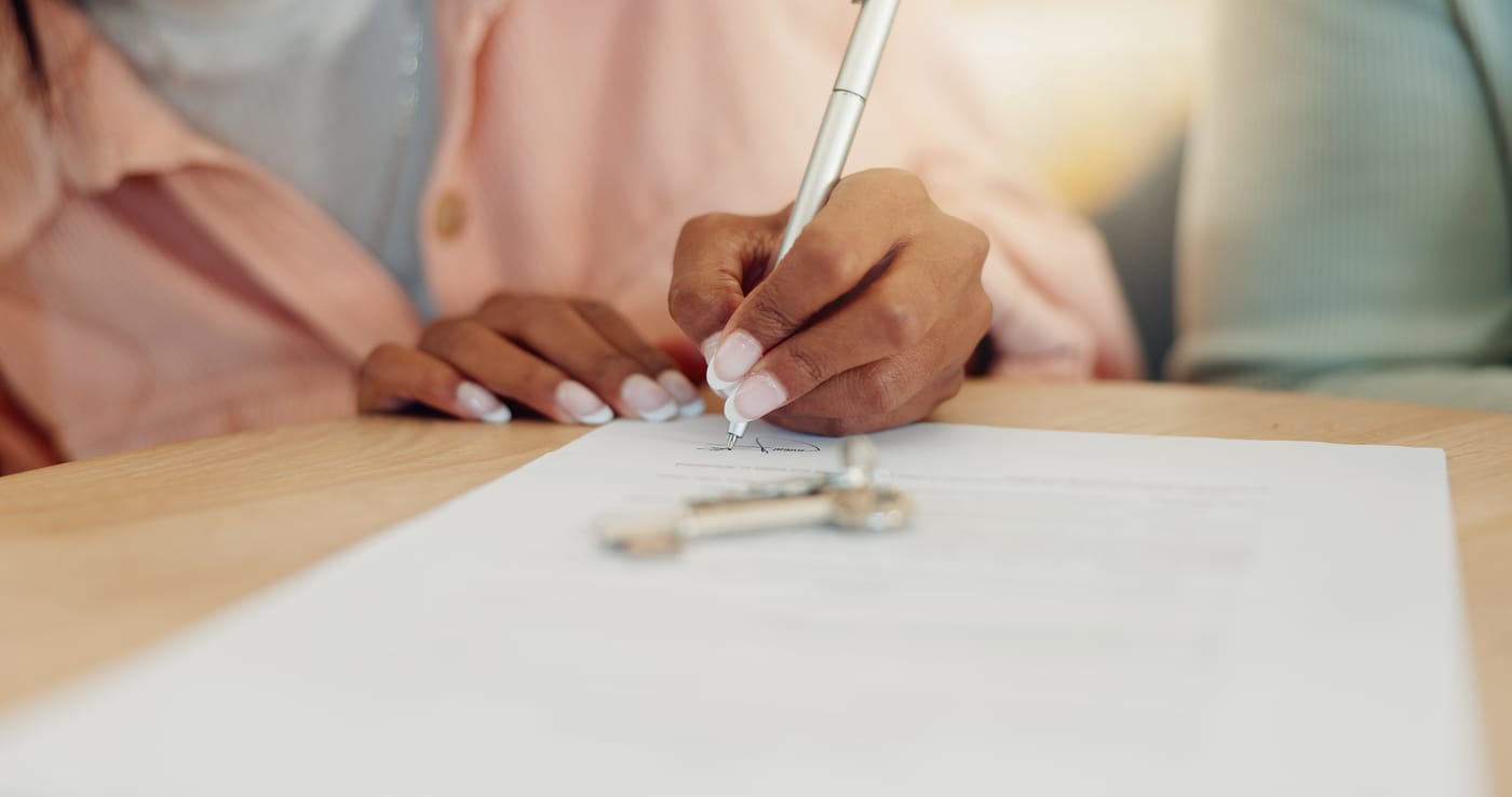 A buyer signing closing documents at a desk with a set of keys nearby.